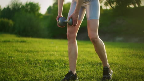 A-young-woman-in-sportswear-leans-forward-with-dumbbells-in-nature-in-a-Park-at-sunset.-Workout.-Work-on-a-beautiful-body-in-the-morning-or-at-sunset